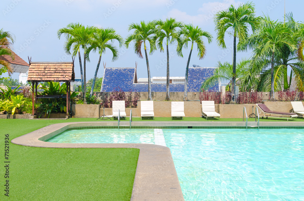 Swimming pool with green grass and palm at hotel close up
