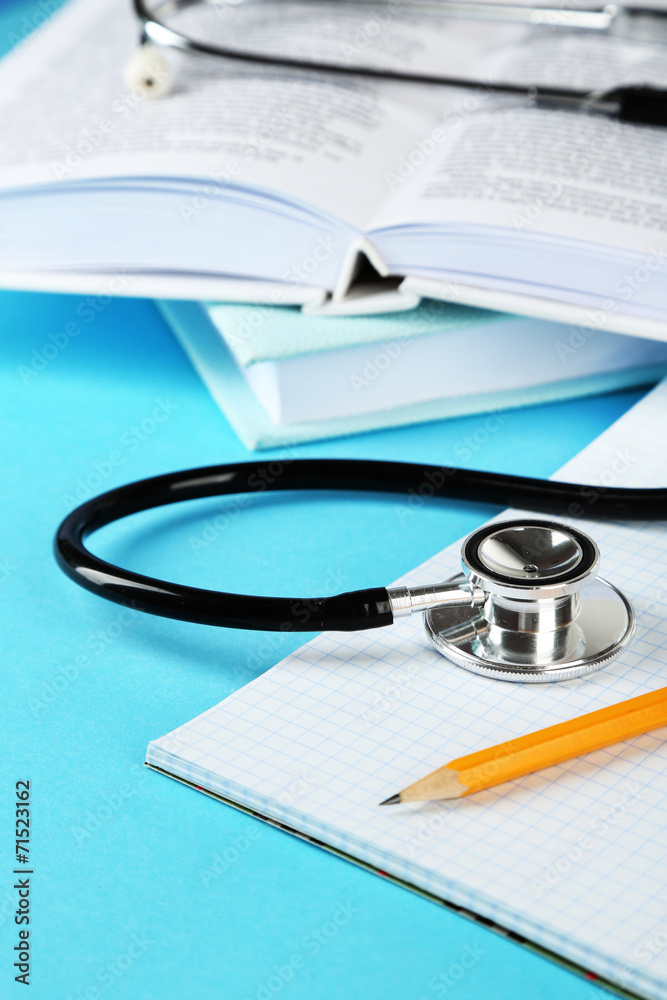 Medical stethoscope with notepad and books on blue background Medical stethoscope with notepad and books on blue background
