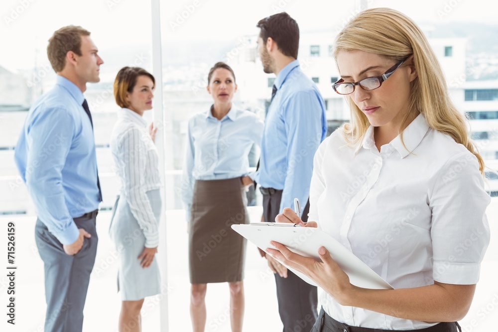 Businesswoman writing notes with colleagues behind Businesswoman writing notes with colleagues behind