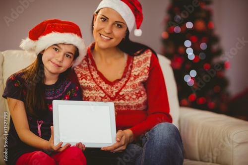 Festive mother and daughter showing tablet screen