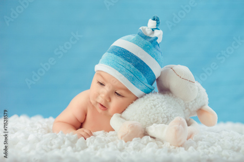 Child in hat hugging toy on a white bedspread, on a blue backgro