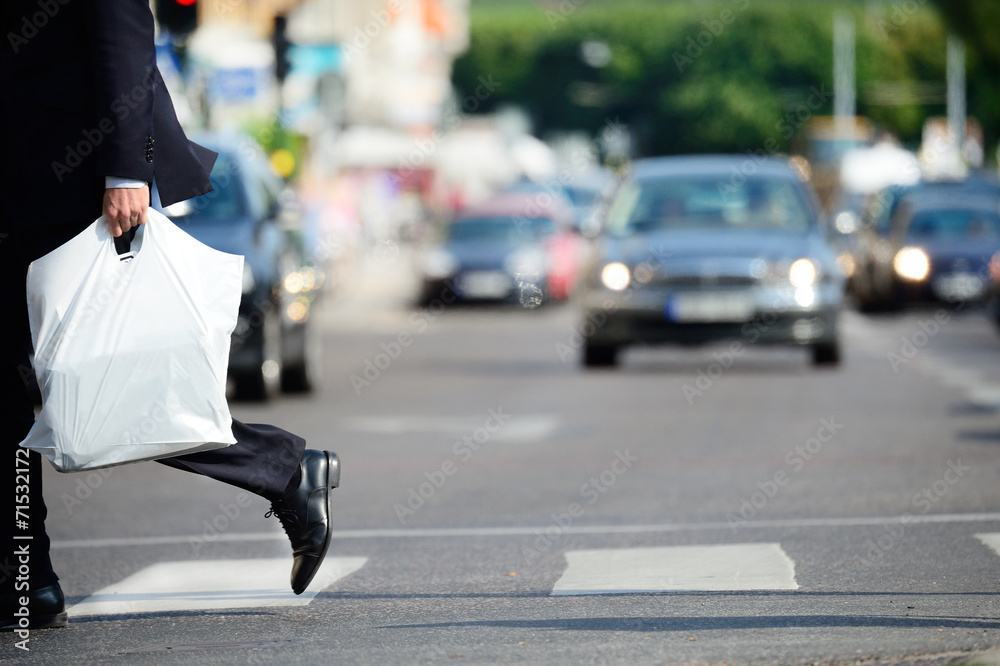 Obraz premium Man in suit with plastic bag crossing street