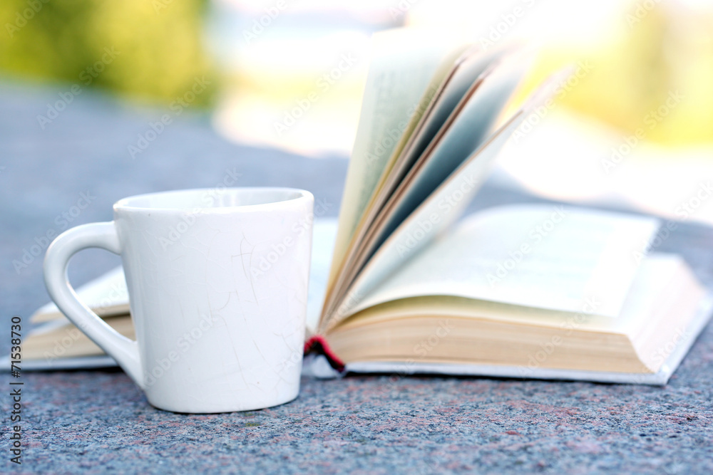 Cup with hot drink and book, outdoors