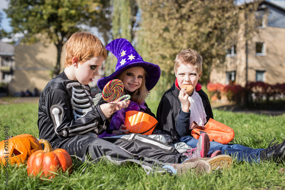 Fototapeta premium cute friends sitting on the grass and eating Halloween candies