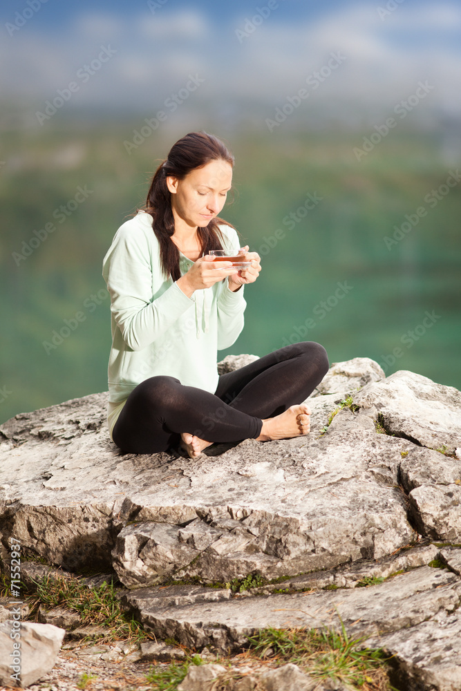 Frau sitzt auf einem Stein und trinkt Tee