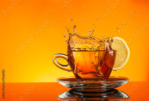 Tea splashing out of glass with orange background