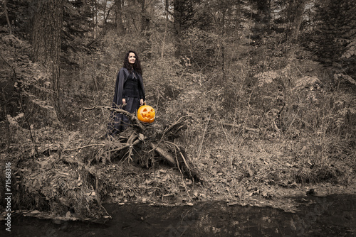 halloween witch with pumpkin by the river, desaturated photo