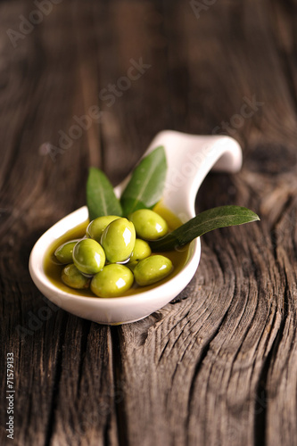 Green olives in the bowl and olive branch on wooden table
