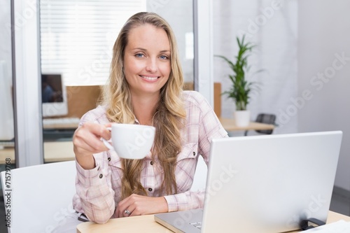 Cheerful businesswoman using her notebook holding a cup