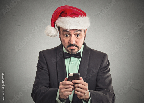 man wearing santa claus hat looking at smartphone shocked © pathdoc