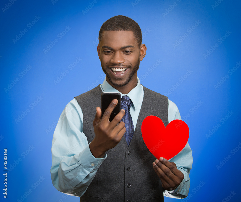 Man looking at smart phone holding red heart blue background Man looking at smart phone holding red heart blue background