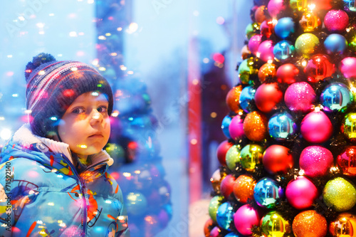 Adorable little boy looking through the window at Christmas deco