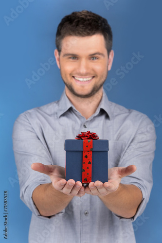 close-up on smiling guy offers gift in blue box. © BlueSkyImages