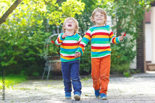 Two little sibling kid boys in colorful clothing walking hand in