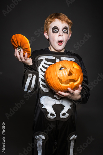 red haired child in Halloween costume holding a orange pumpkin