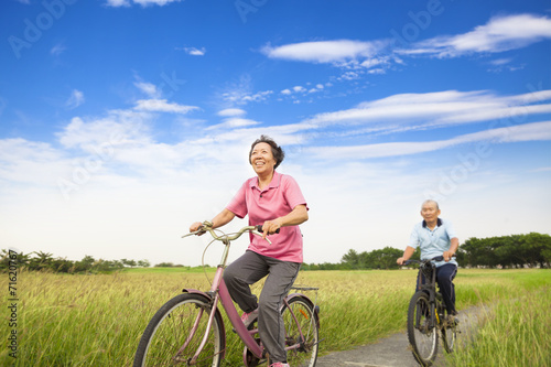 Happy Asian elderly seniors couple biking in farm