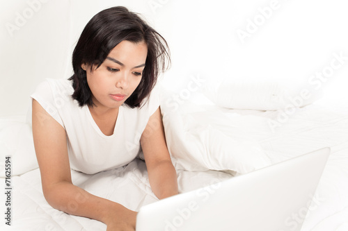 Smiling woman using a laptop while lying on her bed © Nonwarit