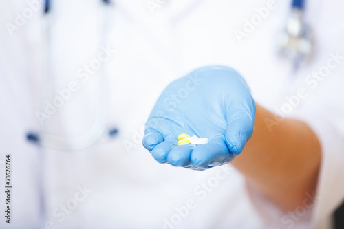 Doctor`s hand in blue glove holding out pills.