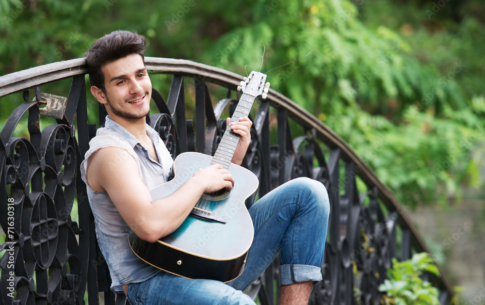 Young guitarist playing on the bridge and smiling at camera