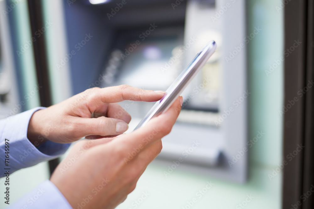 Woman using her mobile phone in front of a cash machine Woman using her mobile phone in front of a cash machine