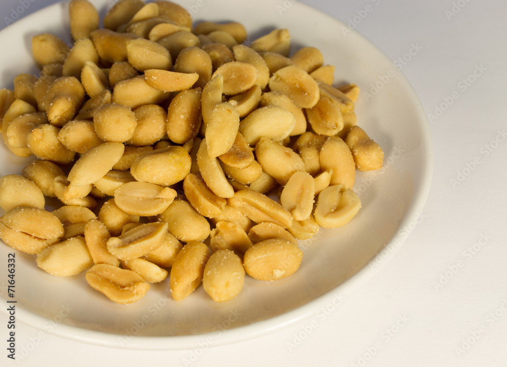 Salty peanuts on a white plate on a white background