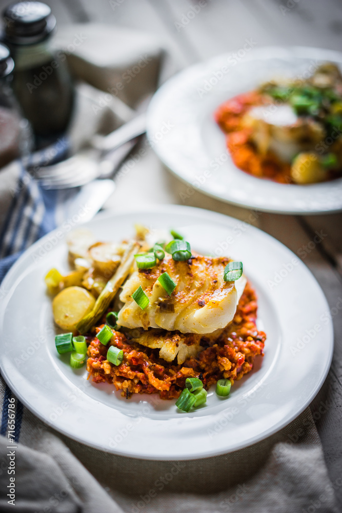 Roasted hake with romesco sauce and onion on wooden background Roasted hake with romesco sauce and onion on wooden background