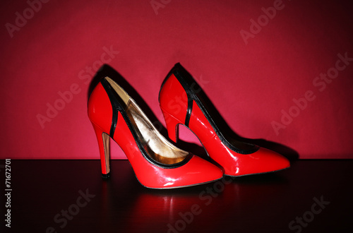 Pair of woman's red shoes on floor on red wall background