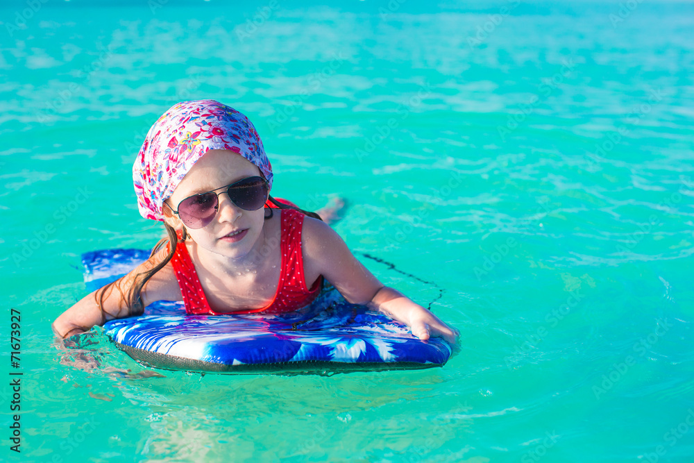 Little adorable girl on surfboard in the turquoise sea