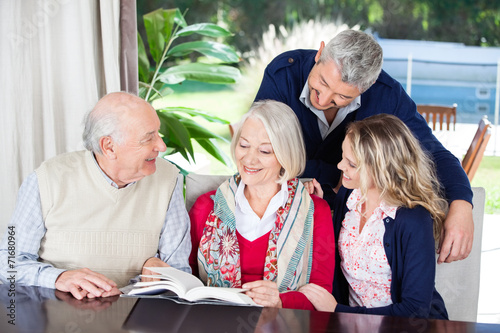 Happy Couple With Grandparents Reading Book In Nursing Home