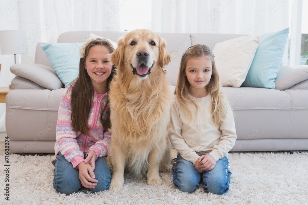 Sisters sitting on rug with golden retriever smiling at camera Sisters sitting on rug with golden retriever smiling at camera