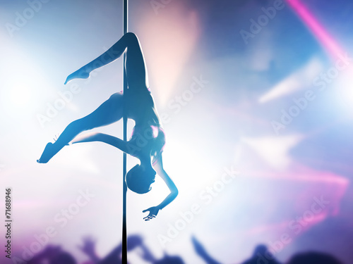 Woman performs pole dance in night club. Sexy body silhouette