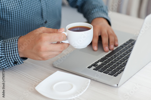 man working at a laptop and drinking coffee