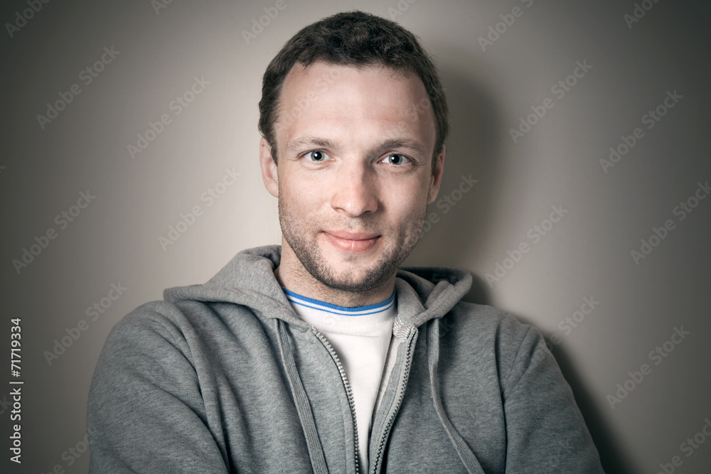 Fototapeta premium Young smiling Caucasian man in gray sporty jacket with hood