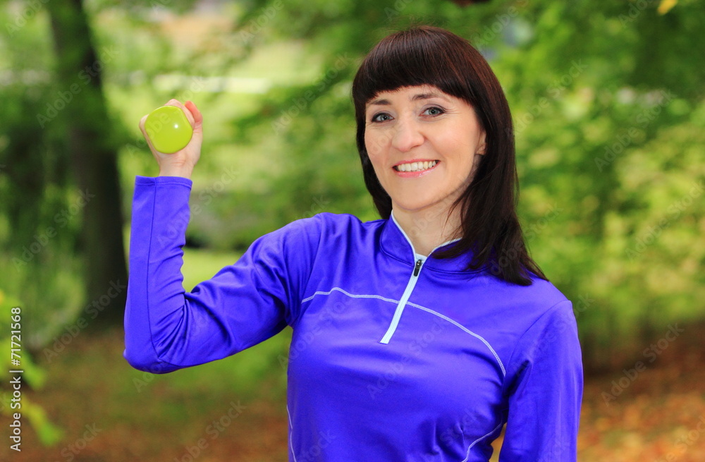 Brunette during fitness exercise with dumbbells in autumn park Brunette during fitness exercise with dumbbells in autumn park