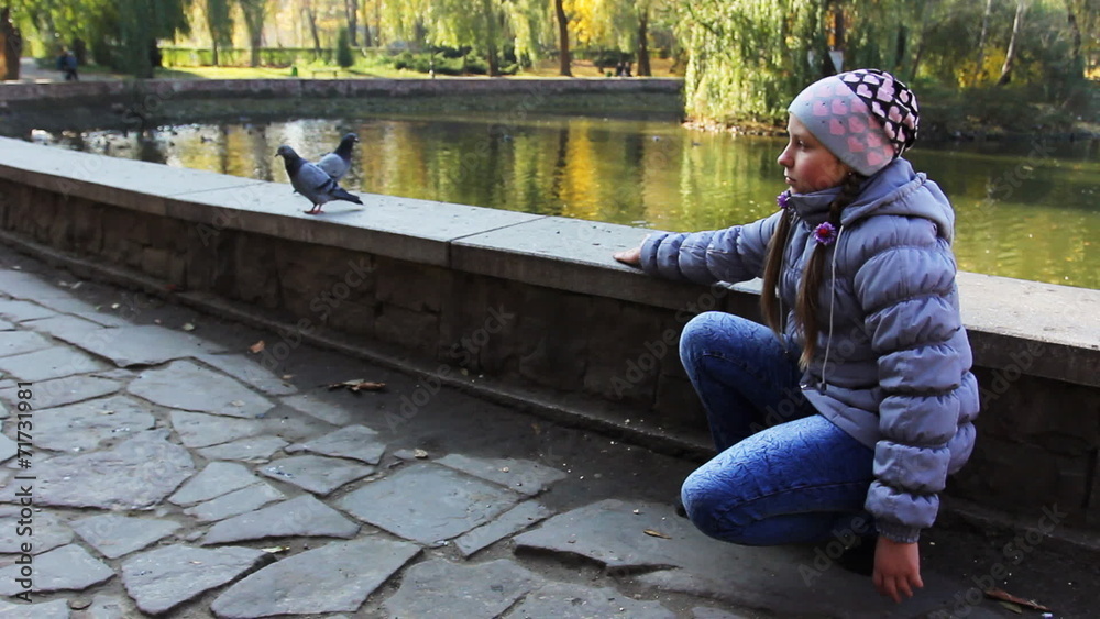 teen girl sits and luring pigeons throwing pop-corn near lake