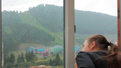 young girl has rest and watching in window on rainy mountains photo