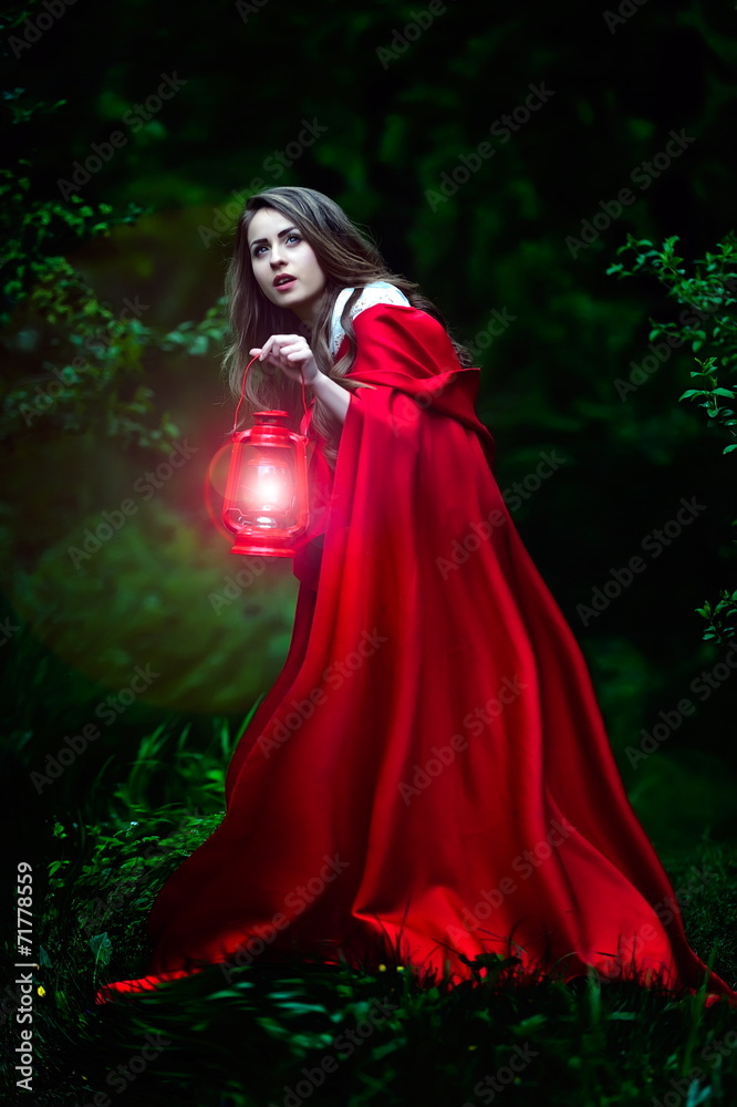 beautiful woman with red cloak and lantern in the woods