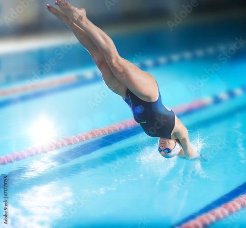Female swimmer, that jumping into indoor swimming pool.