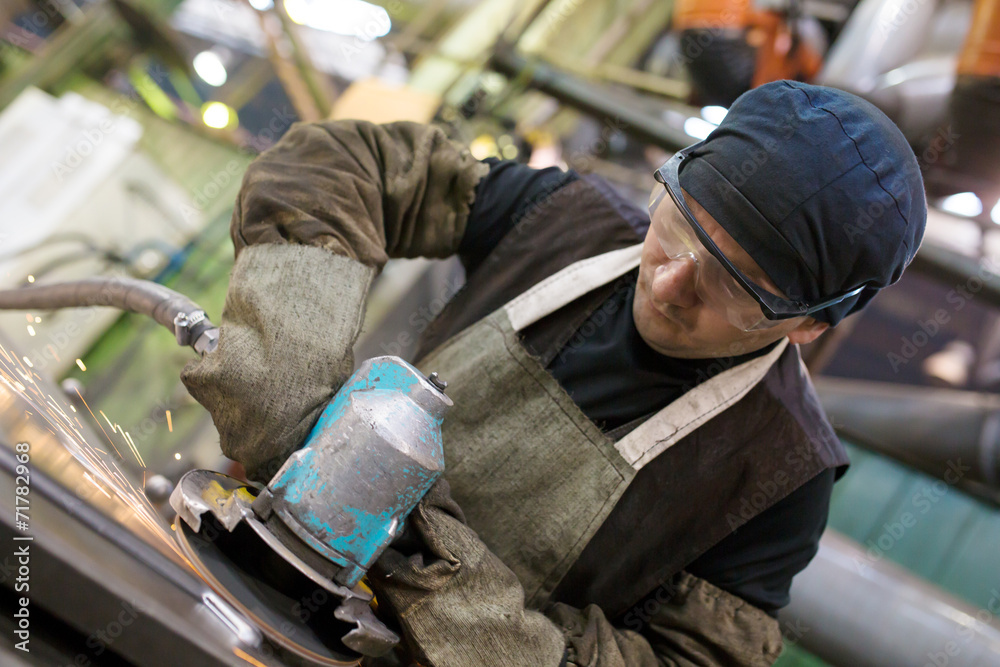 Industrial worker grinding metal sheet with sparks in workshop