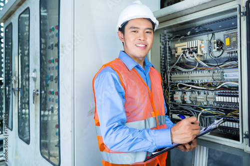 Asian Electrician at panel on construction site