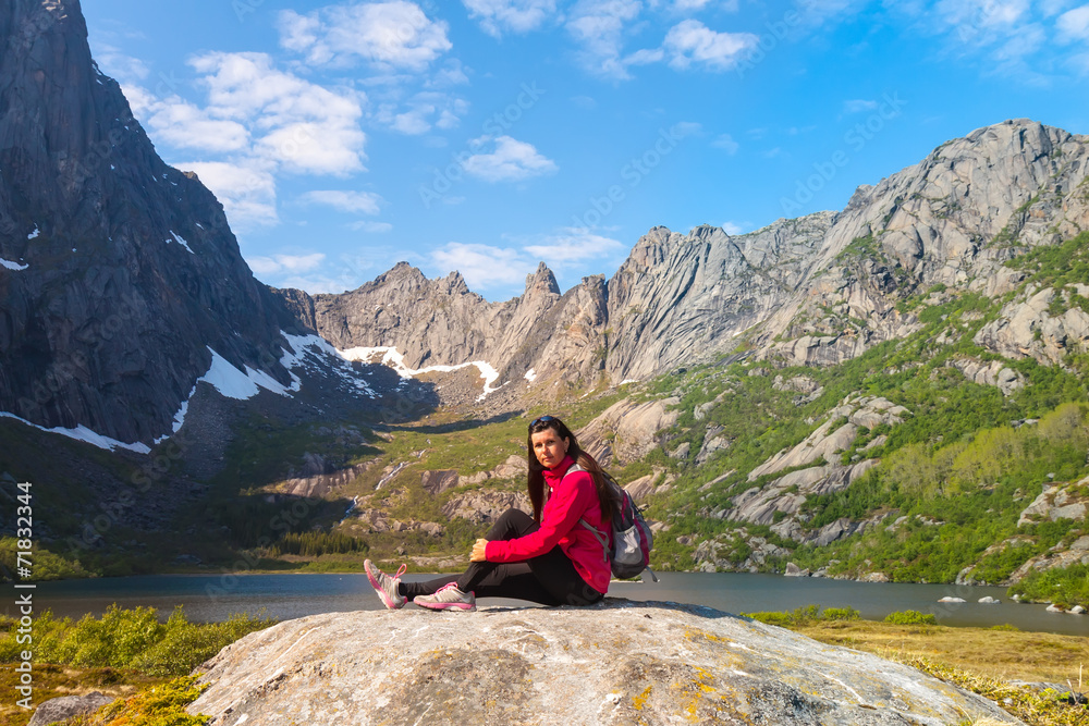 Young tourist woman is sitting on stone near mountain lake Young tourist woman is sitting on stone near mountain lake