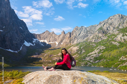 Young tourist woman is sitting on stone near mountain lake