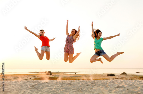 smiling teen girls jumping on beach