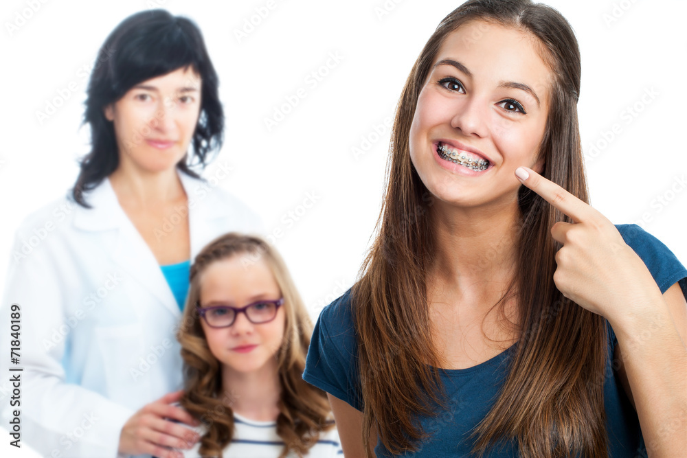 Teen girl pointing at dental barces with doctor in background. Teen girl pointing at dental barces with doctor in background.