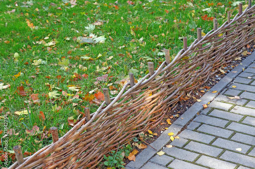 Braided twigs low fence separating diagonally lawn with fallen l
