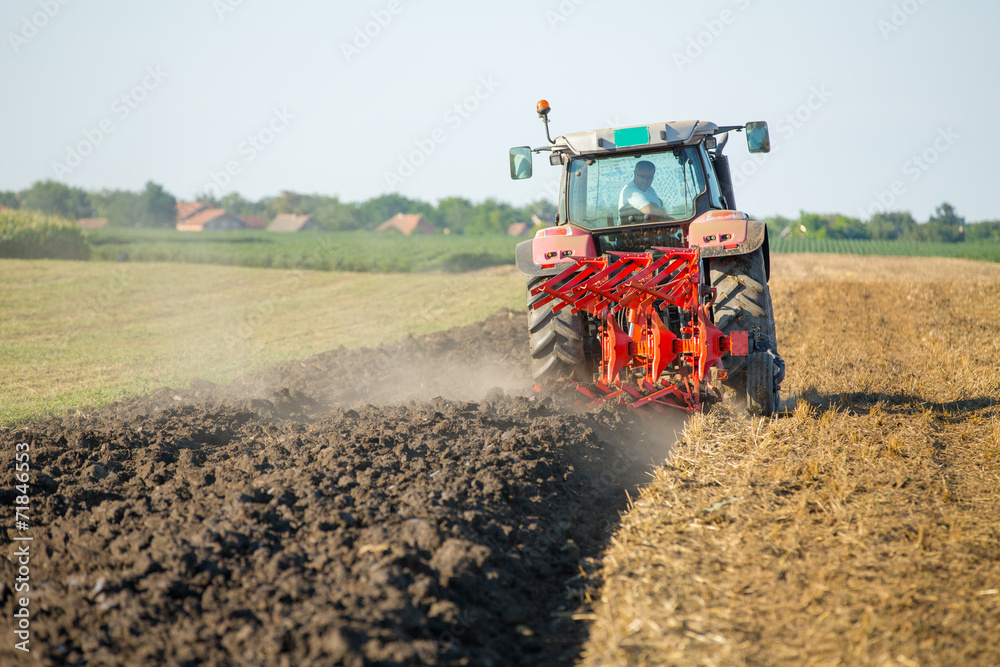 Fototapeta premium Farmer plowing stubble field with red tractor