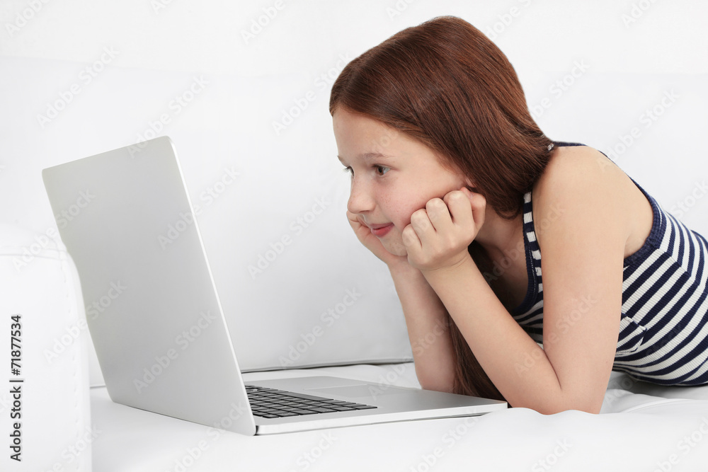 Beautiful little girl with laptop on sofa in room Beautiful little girl with laptop on sofa in room