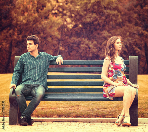 Young couple sitting apart on the bench in the park