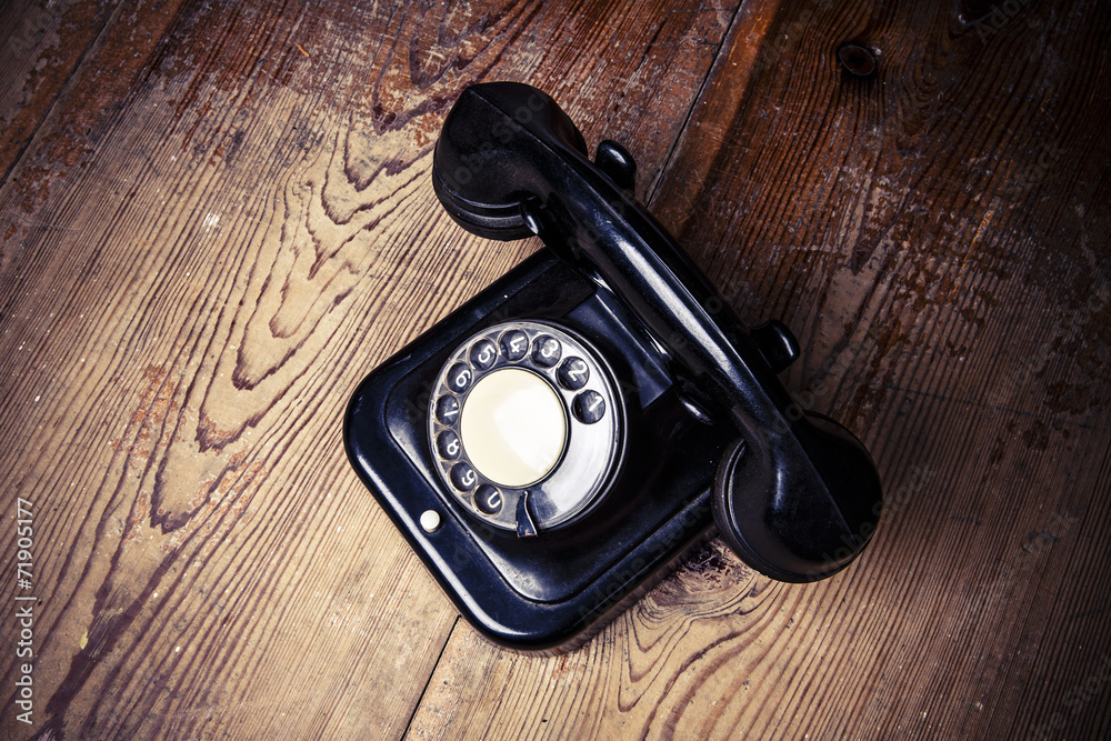 Old black phone with dust and scratches on wooden floor