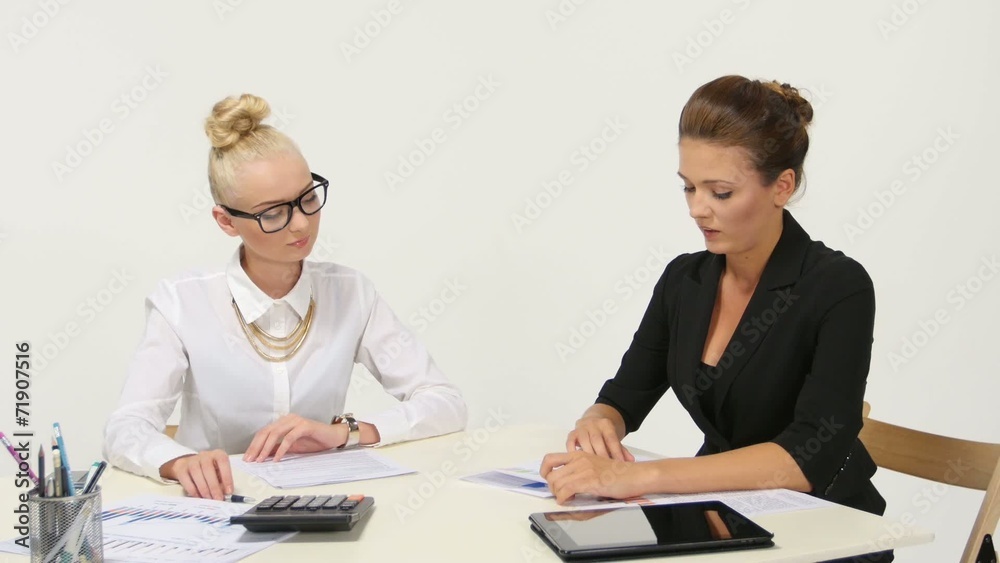 Businesswomen discussing paperwork at office desk. Businesswomen discussing paperwork at office desk.